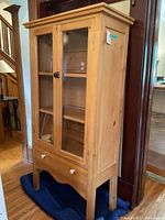 Three-quarter view of entire cabinet showing glass doors, lower drawer, and legs