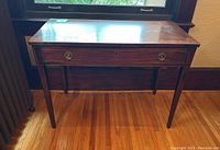 Front angled view of walnut side table showing drawer panel with brass handles and wood grain.