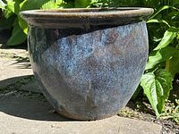 Side view of blue tone ceramic planter showing its shape, glazing, and size relative to background foliage.