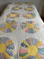 Full view of the handmade quilt showing the bright patchwork flower motifs with yellow centers over a white quilted background on a bed.