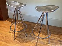 Two stainless steel saddle-seat bar stools side by side on wooden floor