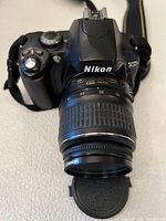 Front view of camera body with Nikon logo and mounted 18-55mm lens, lens cap removed