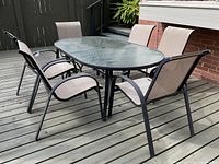 Full view of patio table and six chairs arranged around it on a wooden deck.