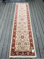 Full view of the long runner carpet laid out on a wood floor, showing the burgundy border, cream central field and overall floral pattern.