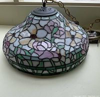 Angle of Tiffany style chandelier showing floral stained glass pattern and dark metal top with chain.