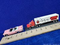 Pink 1958 Buick Century convertible diecast car and red 1996 Red Dog Matchbox semi truck and trailer beside a ruler for size reference.