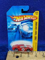 Photo showing front view of the new in package Hot Wheels 2007 First Edition Ferrari 250 LM diecast car with packaging and measurement scale.