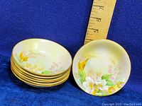 Seven small round hand painted fruit nappies stacked with one bowl displayed next to a ruler showing size approximately 5 inches.
