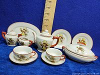 Full tea set items arranged on blue cloth with ruler for size reference.