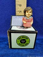 Front view of the figurine standing on the original box with a ruler showing approximately 2.25 inches in height, figurine painted to represent Jacqueline Kennedy Onassis.
