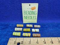 Overview of 10 swirl-patterned cylindrical glass beads and partial card for beading needles with price tag 99 cents.
