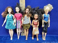Five dolls including four Barbie dolls and one Moana doll with ruler showing height approx 10-12 inches