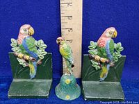 Pair of hand painted metal parrot bookends and a matching metal bell with a parrot figure shown next to a ruler for size reference.