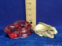 Porcelain and pink glass rabbit figurines side by side with ruler for size reference around 3.5 to 4 inches in length.