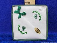 Handkerchiefs folded in box showing white linen with green embroidered clovers and leaves plus green ribbon bow