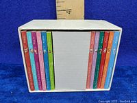 Set of miniature Beatrix Potter books in a white slipcase with ruler showing size, displayed on blue background.