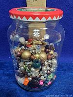 Side view of a glass jar filled with assorted beads and jewelry components showing variety of colors and materials.