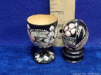 Photo showing the hand painted Russian Khokhloma egg next to the egg cup for scale with ruler background measuring approximately 2.5 inches in height.