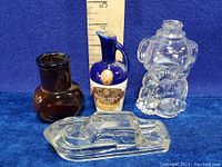 All four items shown together with ruler for size reference: dark brown bottle, cobalt blue liquor bottle, clear glass elephant Bovril bottle, clear glass boat figurine.