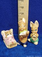 Three hand painted rabbit figurines by Pendelfin on blue background, ruler indicating size around 4.5 inches tall