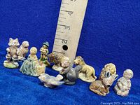 Photo showing a group of 11 small Wade porcelain figurines including animals and human characters with a ruler for size reference on a blue background.