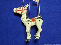 Front side view of white metal horse puppet suspended by control strings on blue background