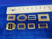 Overview of 8 vintage gold tone belt buckles of various designs and sizes placed next to a ruler for size reference.