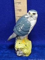Front side view of the ceramic merlin falcon decanter against a blue background, with a measuring scale showing height about 7 inches.