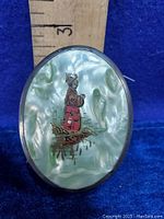 Close-up photo showing hand painted Asian figure on opalescent celluloid top of brush with sterling silver band. A ruler shows the size.