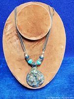 Full view of the vintage necklace with turquoise and bronze tone beads and the round glass pendant on a brown velvet display.
