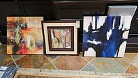 Three abstract prints shown side by side on floor, including two canvas and one framed print