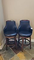 Pair of two wood swivel bar stools with black leatherette seats and backs.