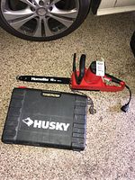 Red Homelite 16 inch chainsaw and black Husky carrying case on floor near tire.