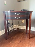 Front view of wooden console table showing two drawers with brass handles and tapered legs with scratches.