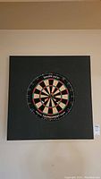 Dartboard mounted on the square black foam protective mat on a wall.