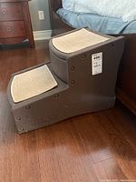 Two step dark brown plastic pet stairs with beige carpeted tread on each step, measuring 16 x 23 x 16 inches.