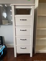 Front view of white laminated dresser cabinet showing four drawers with black handles and an open top shelf