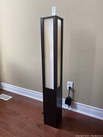 Full view of modern rectangular floor lamp in dark wood finish with white panels, including power cord and plug on floor