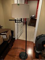 Full view of the floor lamp showing the lamp's base, pole, adjustable arm, and shade in a room.