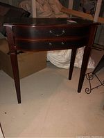 Front view of wood hall table showing single curved drawer with two brass handles and four tapered legs.