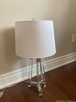 Full view of desk lamp showing white fabric drum lampshade, acrylic legs, and power cord