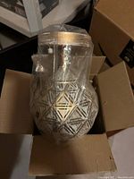Light fixture with geometric etched design wrapped in plastic inside a cardboard box.