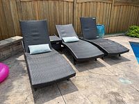 Set of three dark brown PVC woven lounge chairs with blue-grey cushions and a matching side table on outdoor patio near pool and wood fence.