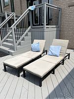 Two resin woven loungers with beige cushions and light blue pillows on painted deck