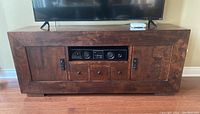 Front view showing dark wooden media cabinet with flat top holding a TV, central electronics device, side doors, and three drawers below.