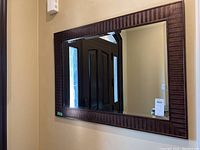 Framed beveled mirror hanging on beige wall reflecting front door and hallway.