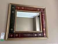 Front view of the rectangular mirror framed with a decorative book spine motif showing colors of red and green with gold detailing.