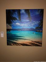 Front view of the 24x24 inch stretched canvas print showing a tropical beach with palm trees, sandy shore and blue ocean under a partly cloudy sky.
