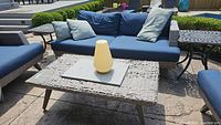 Front view of outdoor sofa with blue cushions and matching wicker-look coffee table