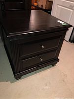 Front view of wood side table showing two drawers with metal knobs and beveled top edge.